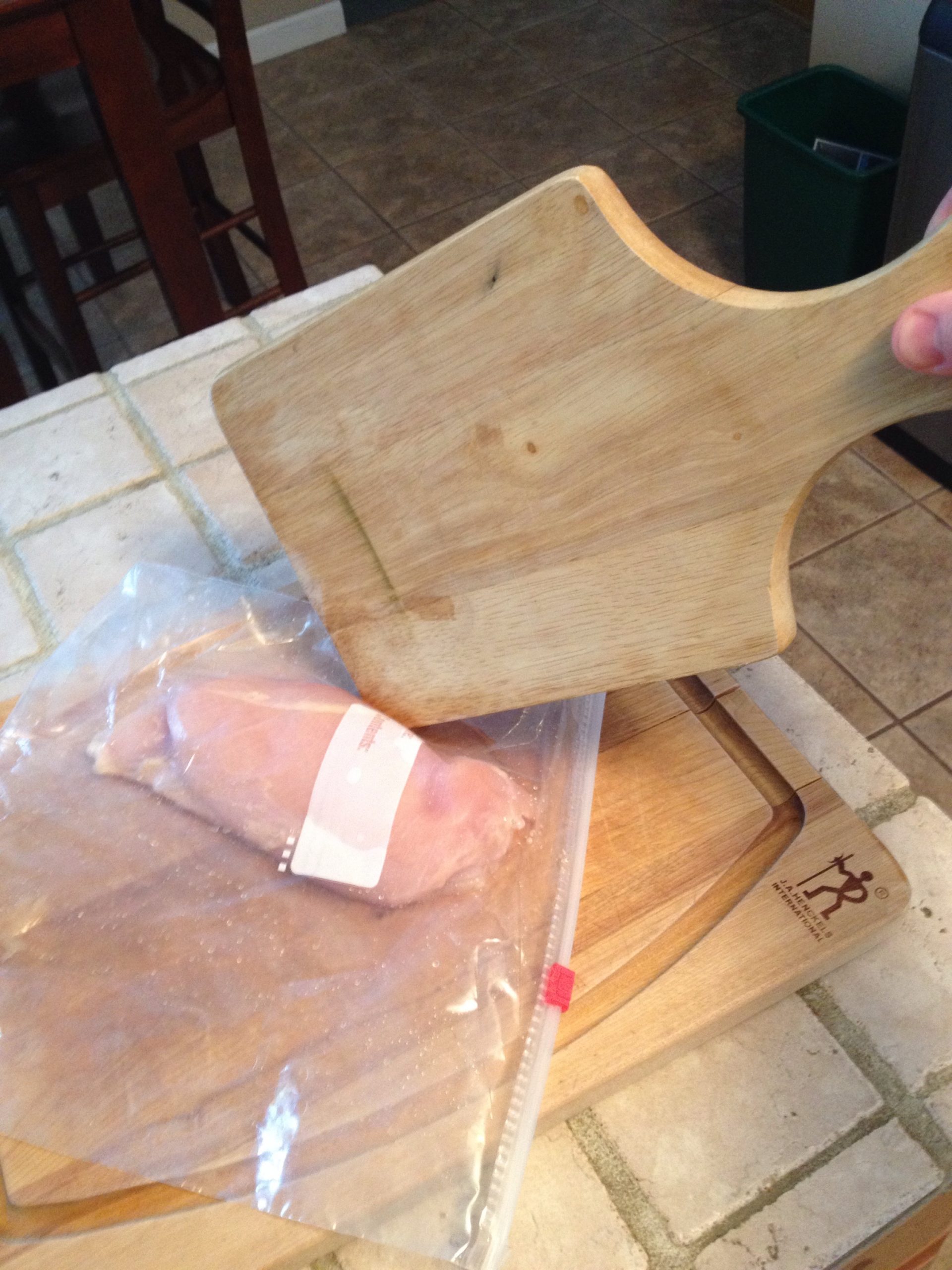 Tenderizing chicken with a paddle cutting board.